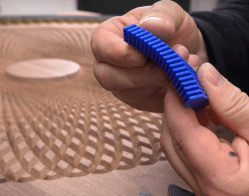 Hands holding a 3d printed sanding block, shaped to fit the grooves routed in the table which is visible in the background.