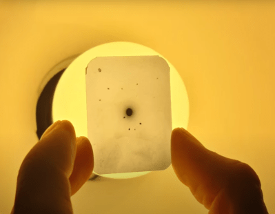 The diffraction pattern generated by a sodium chloride crystal. A slide is shown with a dark black dot in the middle, surrounded by fainter dots.