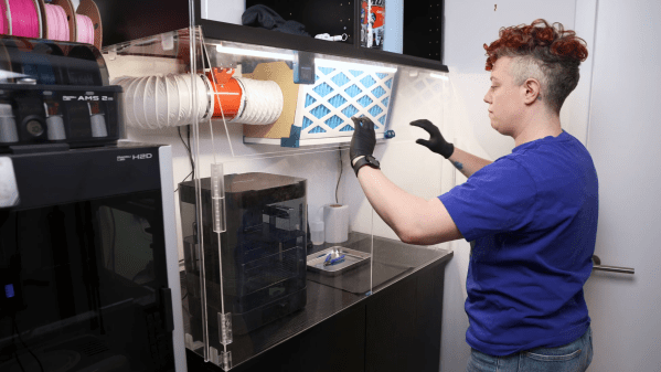 A person is standing in front of an acrylic enclosure, lowering a door on the enclosure. The enclosure contains the space between two sets of cabinets, and has three doors on the front. Inside the enclosure is an air filter and a washing station.