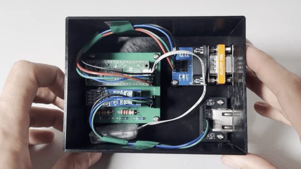 A black plastic box is shown, with a green circuit board inside. The circuit board is wired to an RS-232 connector and an RJ-45 connector.