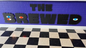The logo for coffee shop "The Brewed" against purple bricks on the front of the front counter.