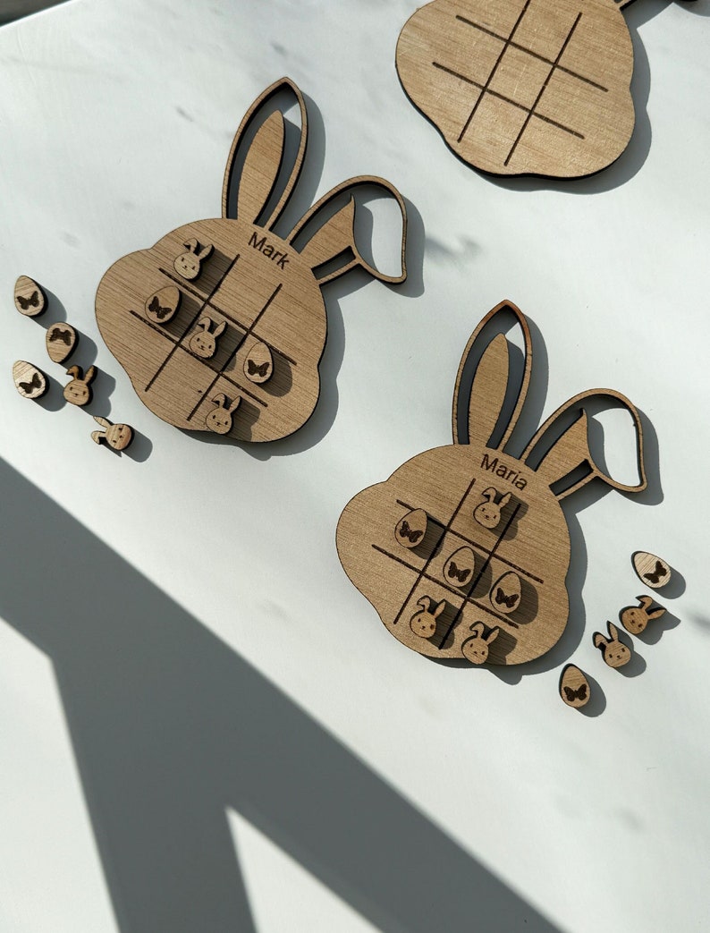 Easter joy meets classic fun with our personalized wooden Noughts and Crosses game shaped like a bunny. Engraved with the name, it comes adorned with Easter eggs and bunnies for playful holiday gaming. EasterGame PersonalizedGift WoodenBunny KidsFun