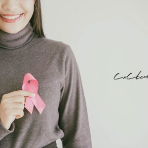 ピンクリボンを胸に当て笑顔を見せる女性