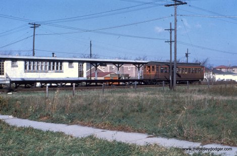 A northbound train at Harrison Street, with new postwar housing in the background. In the foreground, sidewalks that were already about 20 years old go past an empty lot.