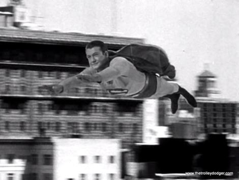 Due to the limitations of 1950s special effects, here Superman is literally "flying by wire." Two wires holding up actor George Reeves are visible against the dark background of Superman's cape.