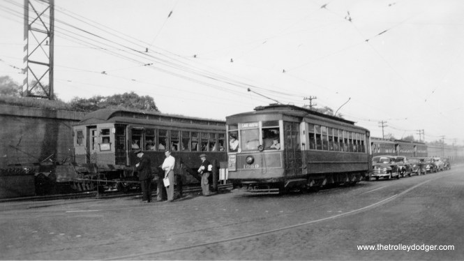 CTA streetcar 1069 is running westbound on Route 16 - Lake Street. Some passengers have just stepped off and are waiting for the gates to go up as a Lake Street "L" train passes. There was a stretch of a few blocks where the ground-level "L" and streetcars ran side-by-side. Here, the trolley is going to go under the nearby embankment to run for a few blocks on the north side of the Chicago & North Western. Streetcars were replaced by buses in 1954, and the "L" was elevated onto the embankment in 1962. The picture can't have been taken before 1948, as the Lake train is a "B." A/B skip-stop service began on the line that year.
