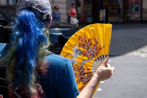 A woman cools herself with a yellow paper fan during a spell of hot weather