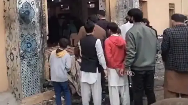 People crowd around the entrance to a mosque that has been hit by an explosion
