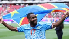 Le joueur congolais Cédric Bakambu célèbre la qualification en coupe du monde avec le drapeau national.