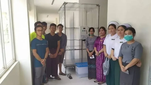 ပလက်စတစ်အကြည်ကို လေးဘက်လေးတန်ကာထားတဲ့ ပိုးသတ်ခန်း ဘယ်ဘက်မှာ ရပ်နေတဲ့ ကျောင်းသား ၅ ဦးနဲ့ ညာဘက်မှာရပ်နေတဲ့ ကျန်းမာရေးဝန်ထမ်း ၅ ဦး