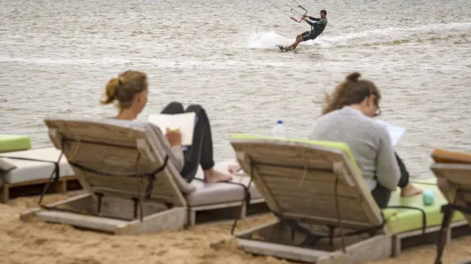 Deux vacanciers européens s'allongent sur des chaises longues au Sahara occidental, tandis qu'un autre fait du kitesurf dans la mer