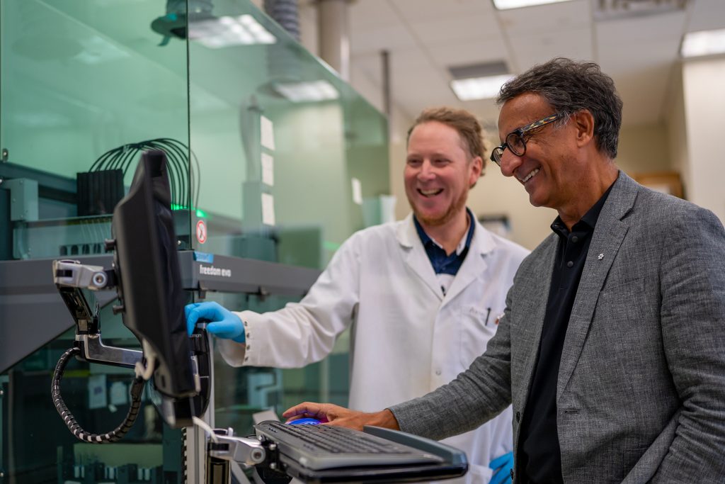 CLSA researchers Alexander Tough and Parminder Raina are smiling while looking at a computer monitor in a lab.