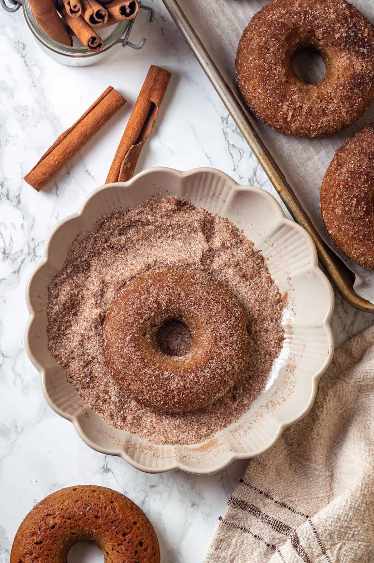 These tender cinnamon-spiced Apple Cider Donuts are baked instead of fried and made without yeast, which means they're super easy to make! Vegan apple cider donuts in plate of cinnamon sugar.