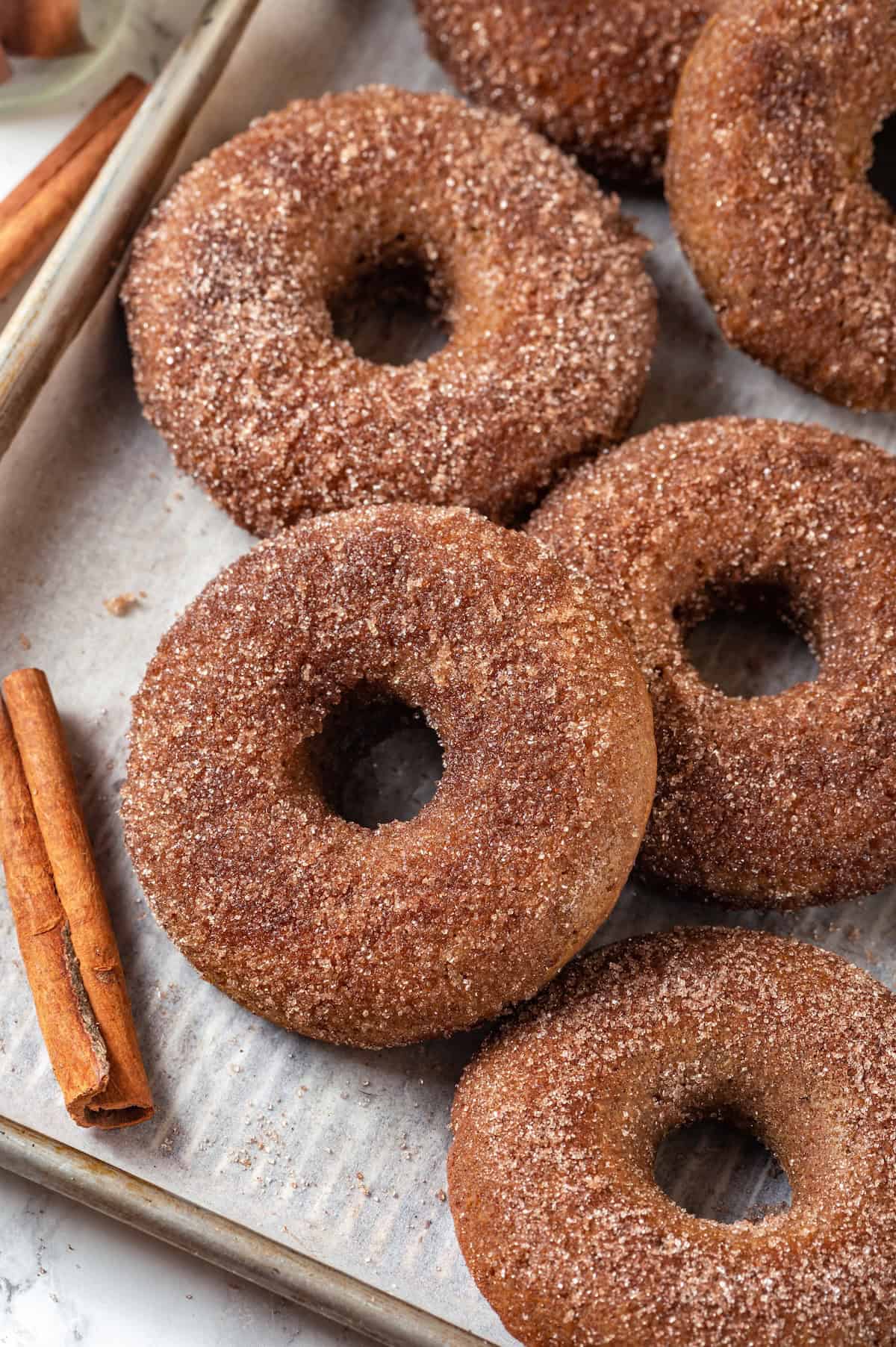These tender cinnamon-spiced Apple Cider Donuts are baked instead of fried and made without yeast, which means they're super easy to make! Baked apple cider donuts on parchment-lined sheet pan.