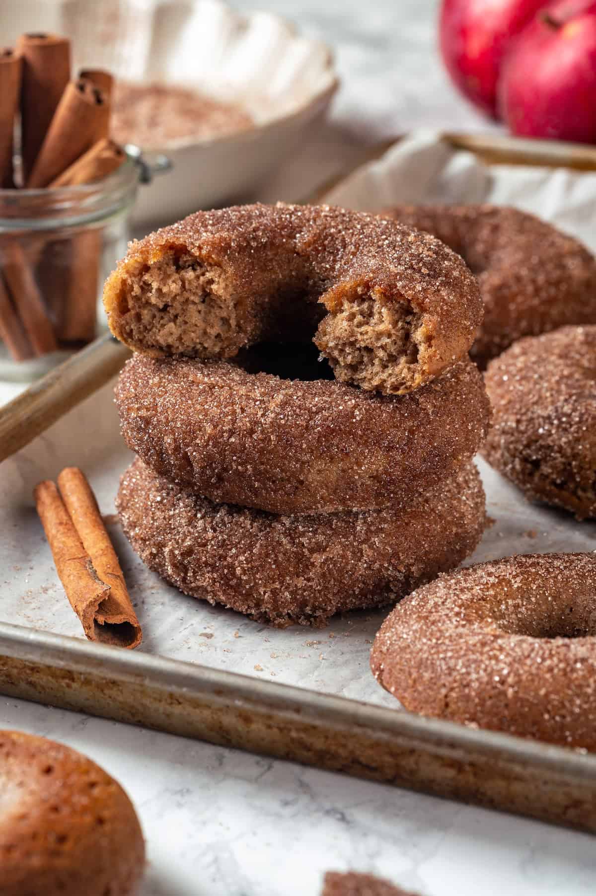 These tender cinnamon-spiced Apple Cider Donuts are baked instead of fried and made without yeast, which means they're super easy to make! Stack of 3 apple cider donuts with top donut broken in half to show tender crumb.