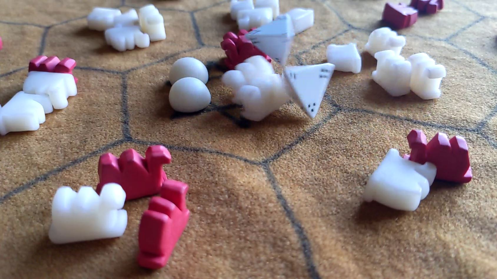 Zwei vierseitige Würfel fallen auf ein braunes Sechseck-Spielfeld mit weißen und roten Kamelen und kugeligen weißen Warensteinen, und werfen dabei zwei weiße Kamele um.