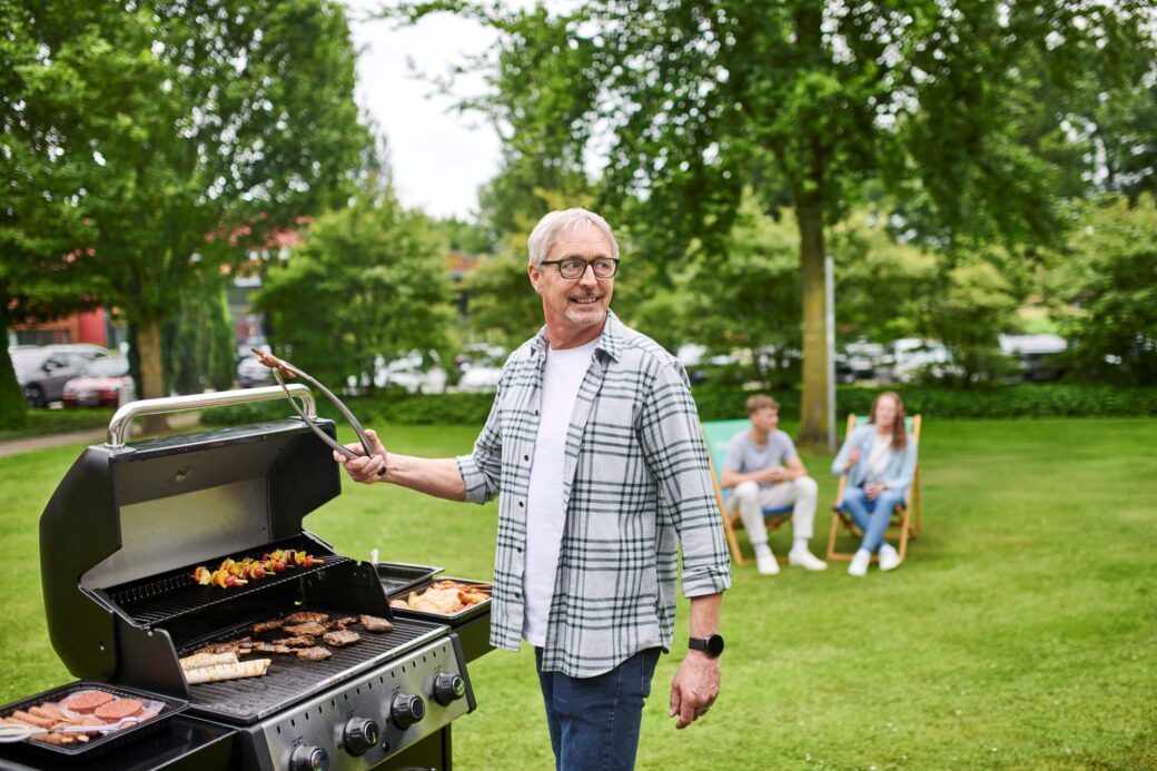 Mitarbeiter dreht sich lachend um, während er mit Grillzange in der Hand am geöffneten Grill steht