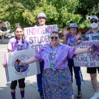 Representatives smiling at a camera holding signs that say 'Indigenous Student Services'