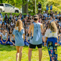 A large group of faculty representatives sitting on the grass listening to a group of faculty representatives.