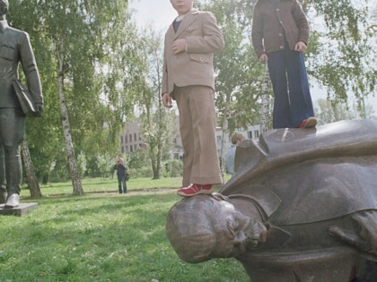 Children stand on a fallen statue of Joseph Stalin.