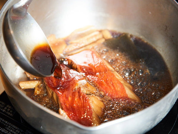 魚に煮汁をかけているイメージ