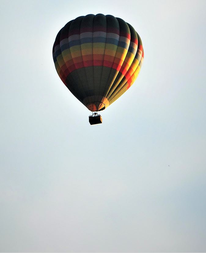 Heißluftballon in Regenbogenfarben (quergestreift), am Himmel von der Abendsonne angestrahlt