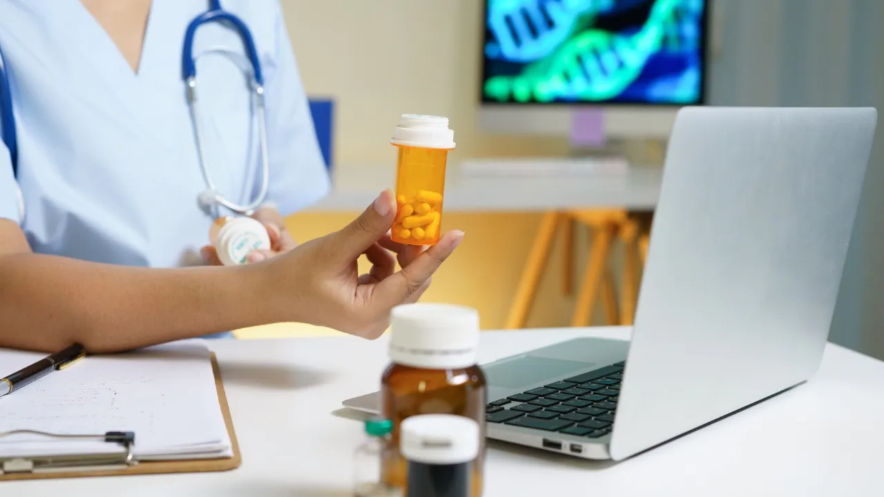 Doctor shows a prescription pill bottle beside a laptop in a telehealth consultation