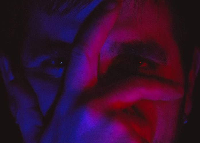 Creative Portrait with Red and Blue Lighting Close-up portrait of a person's face partially covered by their hand, illuminated by red and blue lighting for a dramatic effect.
