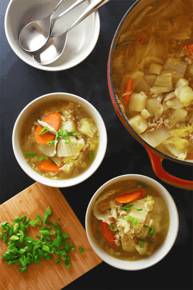 An overhead shot of a tabletop with bowls of Pork and Napa Cabbage Soup