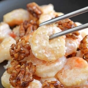 A pair of silver chopsticks picking up Paleo Walnut Shrimp on a black plate.