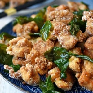 A side shot of a blue plate filled with gluten free and paleo Taiwanese popcorn chicken and fried basil