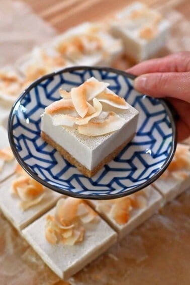 A hand holding a blue and white plate with a coconut cream bar on top.