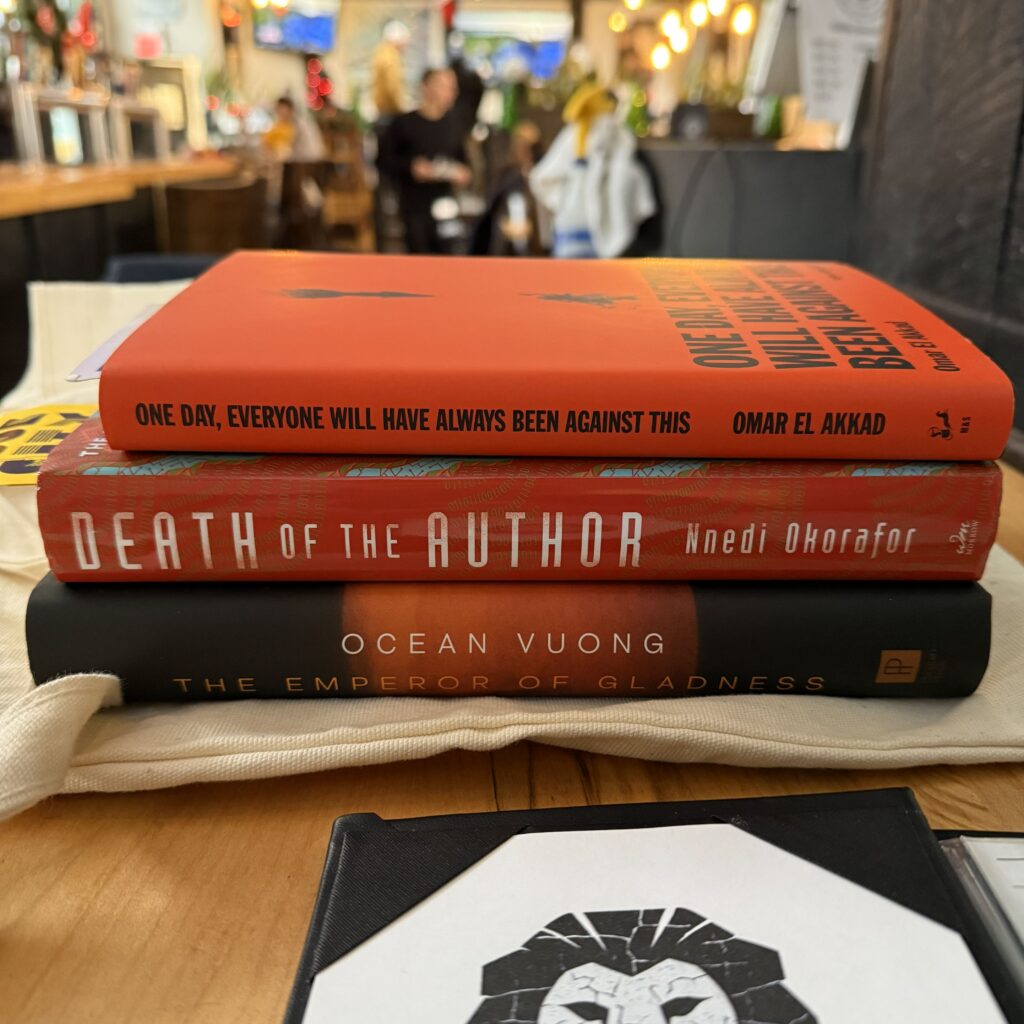 Picture showing hardcover copies of three of my books of the year sitting on a white tote bag on a wooden restaurant table.