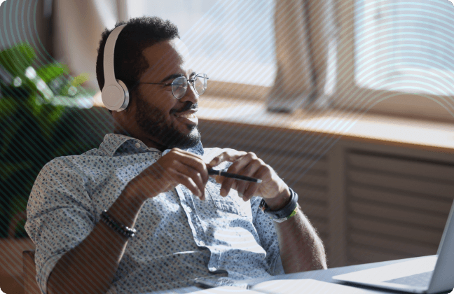 Young man smiling, leaning back in his desk chair with over the ear headphones