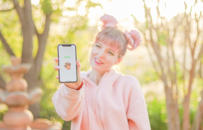 Dave cash advance app review Woman holding phone displaying Dave cash advance app