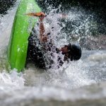 A man makes an eskimo roll in a green kayak