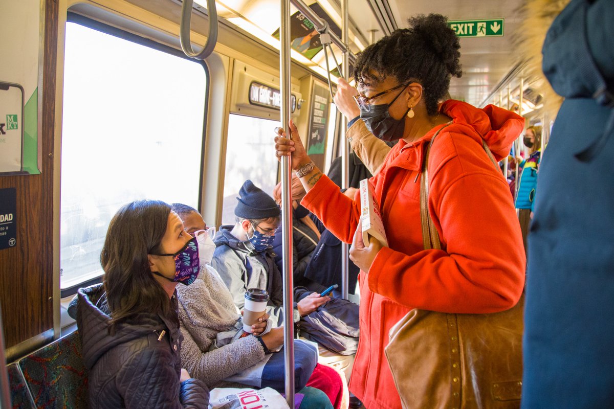 Michelle sits on the Orange Line and looks up to speak with a T rider who is standing in front of her.