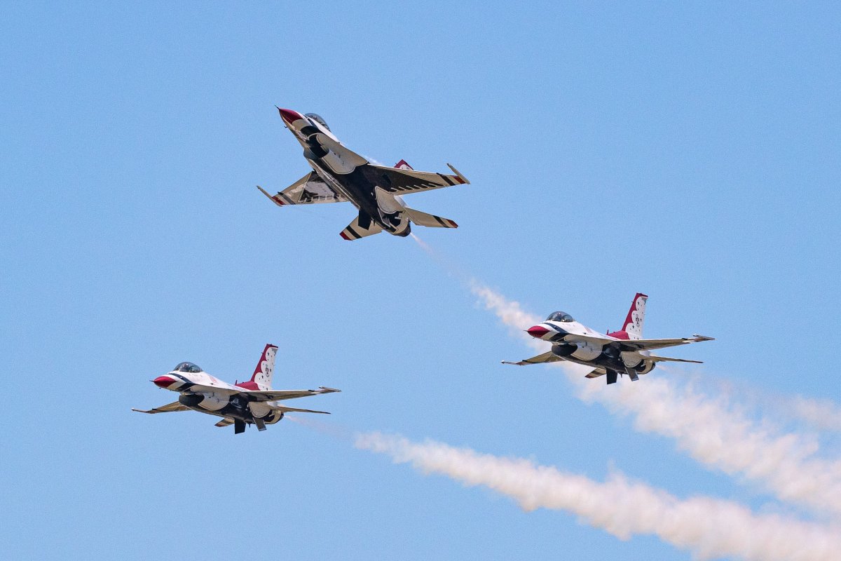Three of the Thunderbird jets fly in a triangular formation against a light blue sky. The jets are red, white and blue, with white contrails trailing behind them. (Photo Credit: NASA/Terry Zaperach)