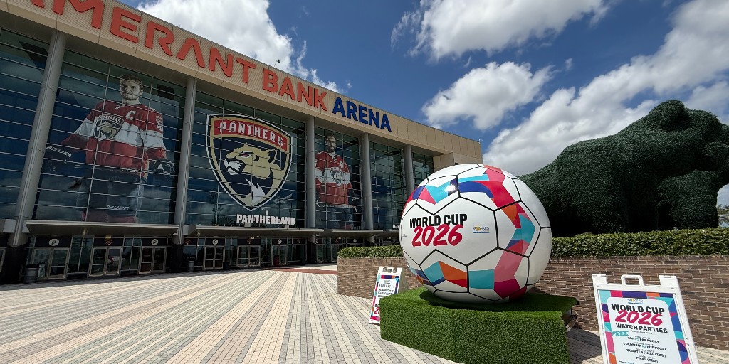 Giant colorful World Cup soccer ball outside an arena titled: Amerant Bank Arena. The ball is on a grassy platform sitting on a brick plaza.