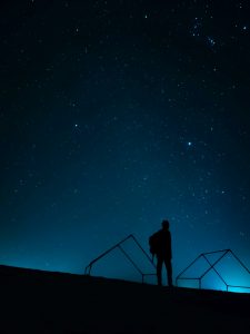 A silhouette of a person standing on a hill against a starry night sky.