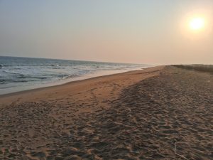 Standing on the beach, the sun is setting in the distance, waves are crashing in.