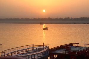 Sunrise view from a dock with some boats in the water and tree lines in the background. Dashassamedh Ghat, Benaras.