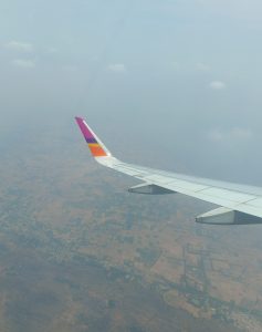 Thai Smile Airways colors on an airplane’s wings flying in the sky. The land and the sky are visible in the background.