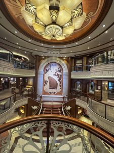 Grand staircase on the Queen Elizabeth cruise ship. Three floors over a large staircase with a mural behind of the ship.