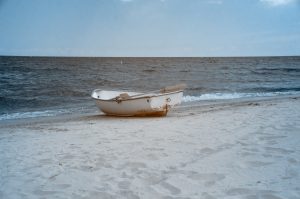 A row boat sits on a beach with light waves on the water and an endless horizon.