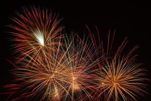 Colorful fireworks explode in the night sky, radiating vibrant streaks of red, orange, yellow, green, and white.