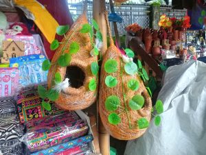 A vibrant display of woven decorative birdhouses shaped like teardrops, adorned with artificial green leaves.