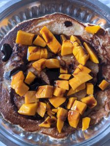 A pancake topped with chopped mangoes and chocolate syrup.