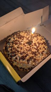 A birthday cake with a lit candle in a box.