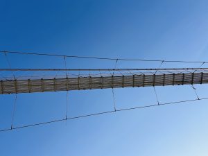 A close-up view of a suspension bridge stretching across a clear blue sky, with cables and supports visible.